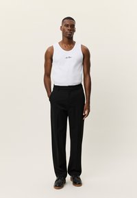 Λευκό αμάνικο με λογότυπο, μαύρο παντελόνι φόρμας και μαύρα παπούτσια. Καθαρές γραμμές και εφαρμοστή σιλουέτα, ομαλή υφή και ουδέτερο χρωματικό συνδυασμό.