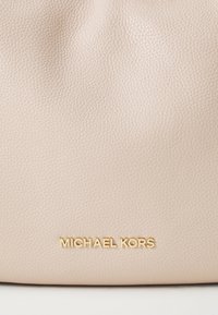 Beige Handtasche aus genarbtem Leder mit glatter Textur und einem goldenen "MICHAEL KORS" Logo in der Mitte unten. Minimales Design mit weicher Struktur.