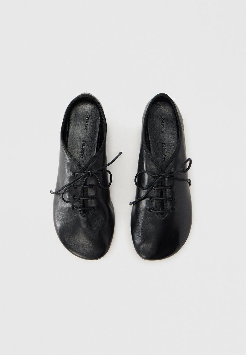 Chaussures en cuir noir avec bout arrondi, semelle plate et design à lacets. Texture lisse avec six œillets et détails minimalistes.