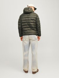 Olivgrüne Puffjacke mit Kapuze, mit horizontalem Steppdesign. Getragen mit hellblauen, ausgewaschenen Jeans und braunen Schuhen.