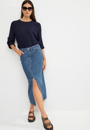 Navy-Bluse mit Drei-Viertel-Ärmeln, kombiniert mit einem mittel langen Jeansrock mit einem Schlitz vorne. Braune Sandalen mit doppelten Schnallen.