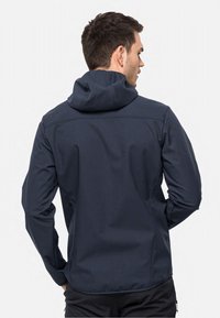 Veste softshell bleu marine avec capuche, présentant une texture lisse et une coupe ajustée, des coutures visibles et un ourlet réglable.