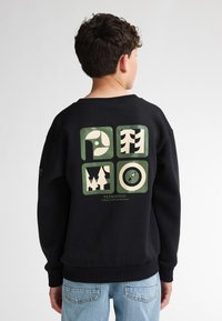 Sweatshirt noir présentant un design graphique au dos, avec des motifs géométriques verts et crème incluant des arbres et une icône.