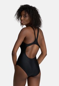 Bañador negro de una pieza con espalda alta y detalles recortados, que presenta tirantes finos y una textura ajustada y suave.