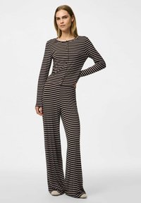 Randig jumpsuit i svart och vitt med långa ärmar, rund halsringning och knappritningar framtill. Den vida designen förbättrar flödet.