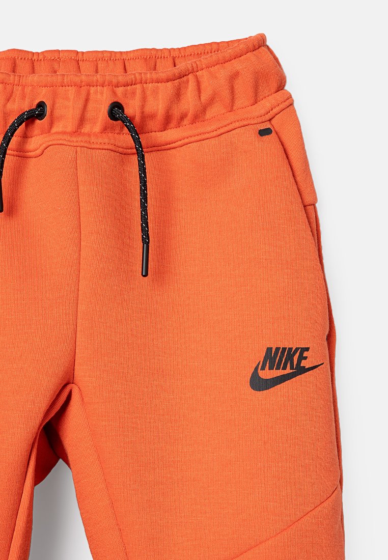 Orangene Nike Jogginghose mit texturierter Oberfläche, featuring ein schwarzes Logo am Bein und einen verstellbaren Kordelzugbund mit schwarzem Kabel.