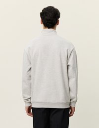 Pelēks vilnas džemperis ar augstu apkakli, ribotiem aprocēm un apakšmalu. Piedāvā brīvu piegriezumu un gludu tekstūru. Parādīts aizmugures skats.