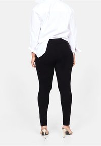 Svarta leggings i stretchmaterial, kombinerade med en vit skjorta med knappar; har hög midja och figurnära passform, med silverfärgade klackar.