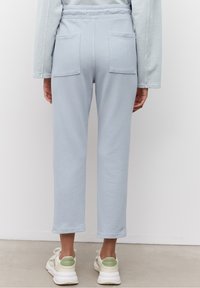 Světlé modré, zkrácené tepláky s elastickým pasem, dvěma zadními kapsami a jemnou texturou. Spárovány s bílými a zelenými teniskami.