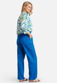 Blouse features a white base with blue and green abstract patterns; paired with bright blue, relaxed-fit pants. Flat sandals complete the look.