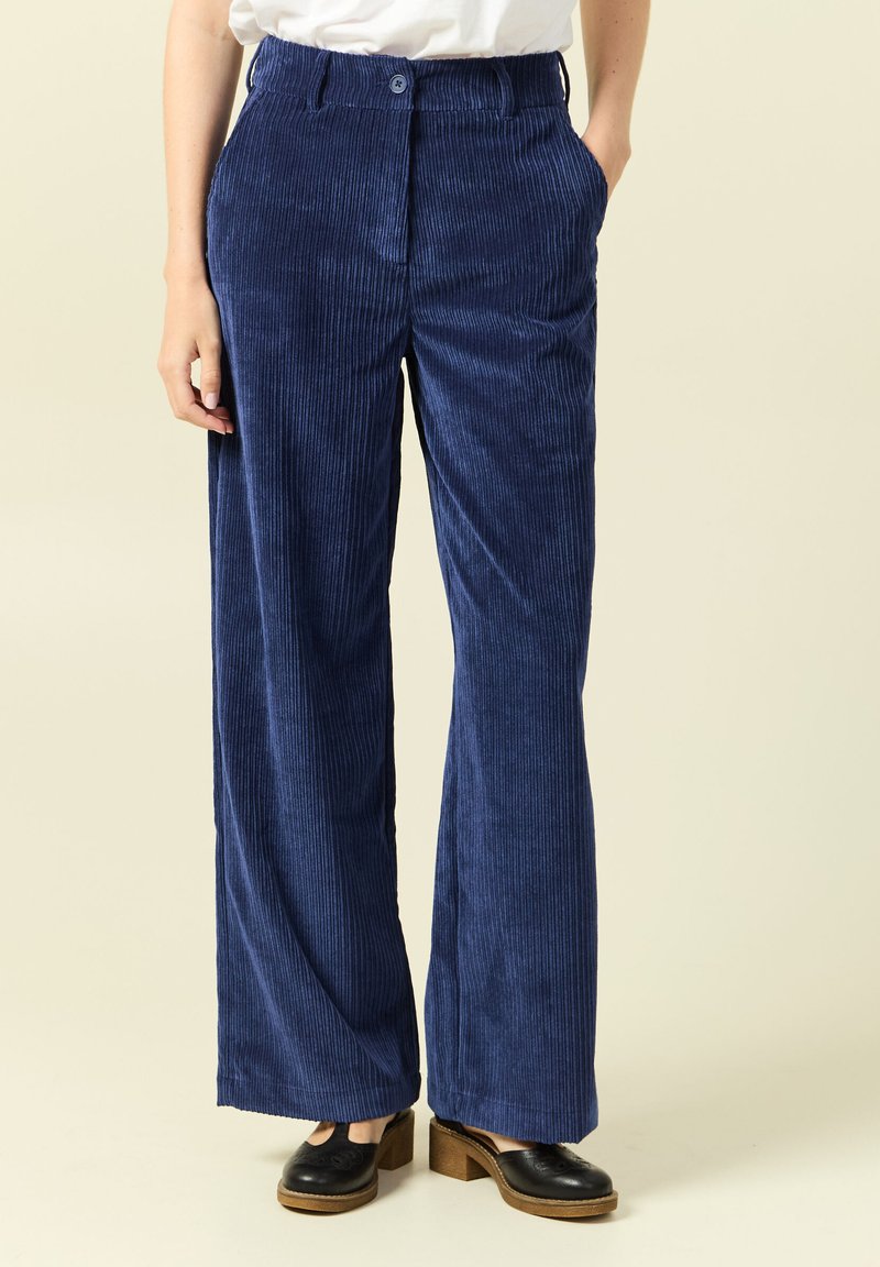 Mörkblå kordfläta byxor med vida ben, framfickor och knappstängning. Texturerat tyg med vertikala räfflor.