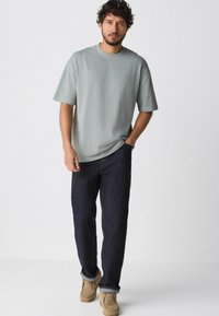 Lys grøn oversized t-shirt i blød bomuld, parret med mørkeblå jeans og beige fodtøj. Simpelt design med en afslappet pasform.