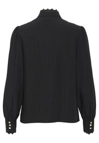 Blouse noire à manches longues, avec un col festonné et un tissu texturé. Des boutons sur les poignets ajoutent des détails au design.