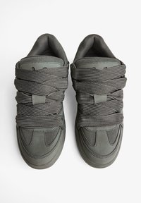 Sivé tenisky s hladkým koženým a textúrovaným sieťovaným zvrškom. Hrubé sivé šnúrky sú pevne tkané okolo tela topánky. Zaoblený dizajn špičky.