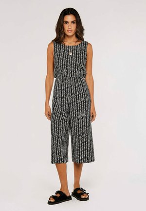 Black and white patterned jumpsuit with herringbone design, sleeveless, relaxed fit, cropped length, cinched waist, worn with black slide sandals.