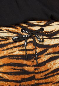 Tijgergestreepte shorts van oranje en zwarte stof met een tailleband met trekkoord. Voorzien van "SPORTS" branding op het trekkoord. Zachte textuur.