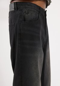 Črne denim hlače ravnega kroja, s petimi žepi, teksturiranim pasom in subtilnim učinkom zbledelosti na blagu.