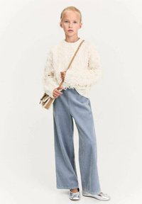 Pulover alb texturat cu margini desfăcute, pantaloni largi cu dungi ribbed de un albastru deschis și balerini metalici argintii. Posetă mică maro pentru umăr.