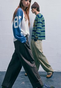 Cămașă cu mâneci lungi, cu mâneci albastre și corp alb, având numărul 87, asortată cu pantaloni largi, de culoare închisă. Poartă încălțări verzi și maro.