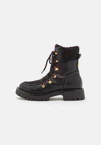 Des bottes noires à lacets présentent un corps en cuir, un col noir duveteux, des accents en métal doré et une semelle épaisse et crantée pour plus de stabilité.