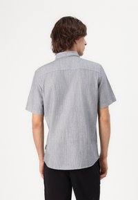 Chemise à manches courtes, avec col, en tissu gris texturé avec des accents bleu clair, présentant un ourlet incurvé et un design de yoke au dos.