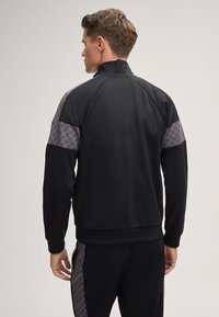 Zwarte sportjack met een hoge kraag, met grijze gemarmerde schouderaccenten en geribbelde manchetten. Glad stof, aansluitend ontwerp.