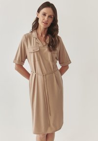 Beige košilové šaty z měkkého materiálu, s límečkem, krátkými ohrnutými rukávy, předními kapsami a stahovací pasem pro úpravu.