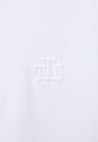 Tissu blanc avec un logo en relief subtil composé de trois formes rectangulaires verticales disposées côte à côte.