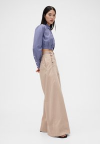 Vyötäröltä korkeavyötäröiset, leveät vaaleanbeiget housut yhdistettynä lyhyeksi leikattuun sinivalkoraidalliseen nappipaitaan, jossa on edessä nappikiinnitys ja sileä pinta.