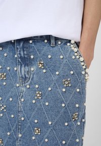 Denim skirt featuring a quilted pattern, embellished with pearls and rhinestones, in light blue with a fitted cut and side pocket detail.