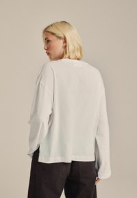 Witte langemouwshirt met een ontspannen pasvorm, ronde halslijn en verlaagde schouders, gecombineerd met zwarte broek. Zachte katoenen stof.
