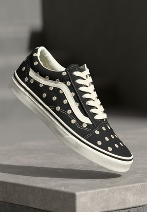 Black canvas sneakers adorned with small white and yellow floral patterns, featuring white laces and a classic rubber sole.