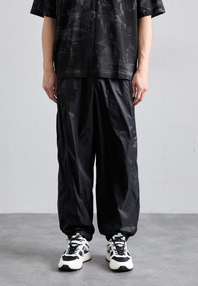 Schwarzes kurzärmliges Hemd mit strukturiertem Muster, kombiniert mit lockeren schwarzen Hosen. Mit elastischen Bündchen und klobigen schwarz-weißen Sneakers.