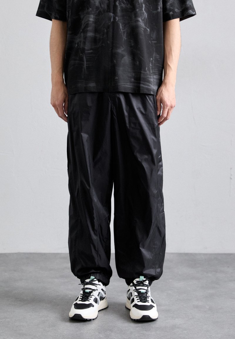 Zwarte korte mouwen shirt met een gestructureerd patroon, gecombineerd met losse zwarte broeken. Beschikt over elastische mouwen en stevige zwart-witte sneakers.