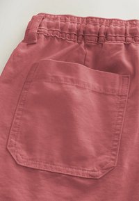Gros plan sur un pantalon en tissu rose montrant une taille élastique et une poche arrière cousue.