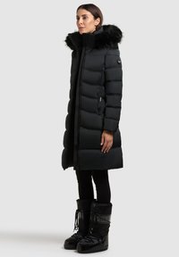 Svart puffig parka med konstpäls på huvan, dragkedja fram och två sidofickor med dragkedja. Matchas med svarta vattentäta vinterstövlar.