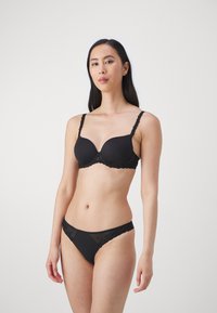 Ensemble de lingerie noir comprenant un soutien-gorge rembourré lisse avec des accents en dentelle et un thong assorti. Le tissu est doux et extensible, avec des détails délicats.
