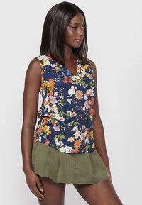 Mouwloze bloemen top met een V-hals; heeft een navy achtergrond met meerkleurige bloemen; lichte stof; ontspannen pasvorm.