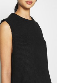 Svart ärmlös stickad topp med en ribbad textur och rund halsringning, med en något lös passform och rena kanter.
