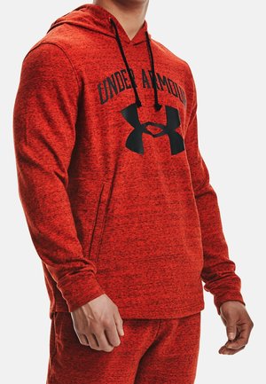 Man wearing red Under Armour hoodie and matching pants, showing the brand logo and front pocket on the hoodie.