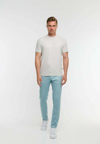 Világosszürke, rövid ujjú póló, amelyhez puha, világoskék leggings és fehér sportcipő társul, egy álló férfi modellen bemutatva.