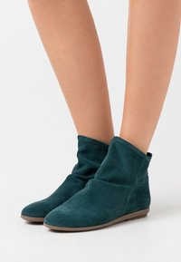 Teal ruskinds ankelstøvler med slaskedesign, rund tå og flad gummisål. Syningsdetaljer langs kanterne.