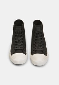 Crne visoke tenisice s glatkim platnenim gornjim dijelom, ravnim crnim vezicama i bijelim gumennim čelom i potplatom. Teksturirani potplat s utorima.