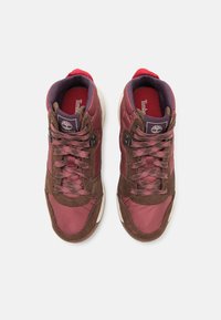 Red and brown high-top sneakers with textured fabric, padded collar, and dark laces. Logo on tongue; contrasting white sole.