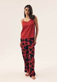 Red satin camisole with thin straps, paired with red pants featuring large black heart patterns, smooth texture, relaxed fit.