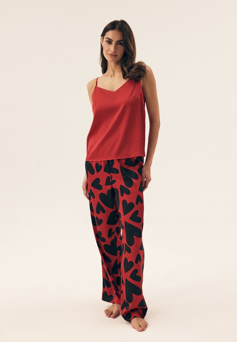 Red satin camisole with thin straps, paired with red pants featuring large black heart patterns, smooth texture, relaxed fit.