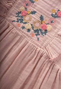 Rotes Stoffkleid mit gestickten Blumenmustern in Gelb, Pink und Blau. Verfügt über einen Rüschenausschnitt und eine geraffte Rockstruktur.