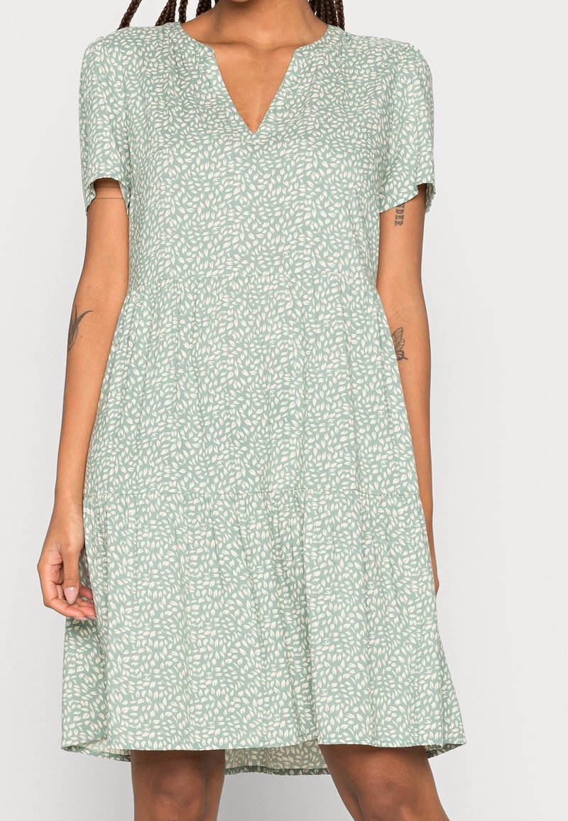 Vestido de manga corta en tela verde clara con un estampado de hojas, presentando un escote en V y una falda acampanada. Textura suave y diseño casual.