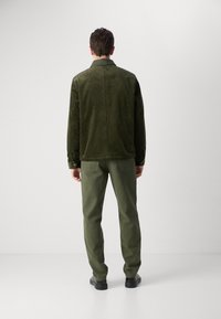 Olive green corduroy jacket with a straight cut, paired with matching green trousers, worn with black shoes, viewed from the back.