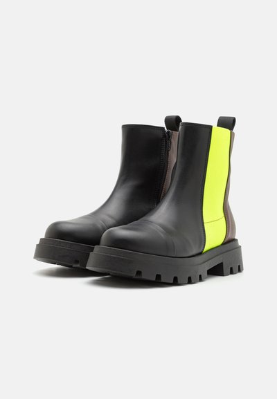 Stivali alla caviglia in pelle nera con una suola spessa nera, dotati di chiusura con zip e un pannello giallo brillante e marrone sui lati.